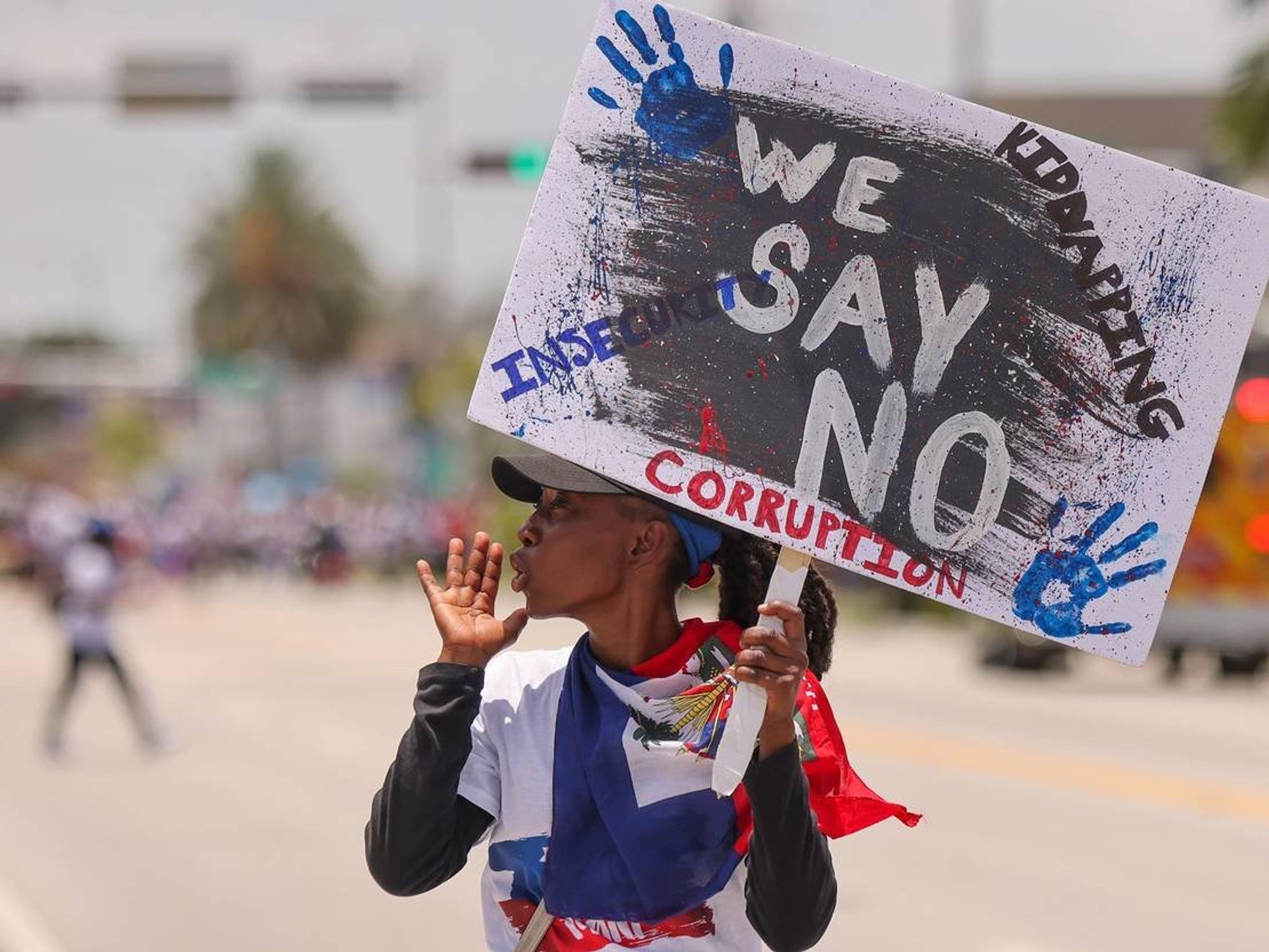A person with a haitian flag around their neck holds a protest sign