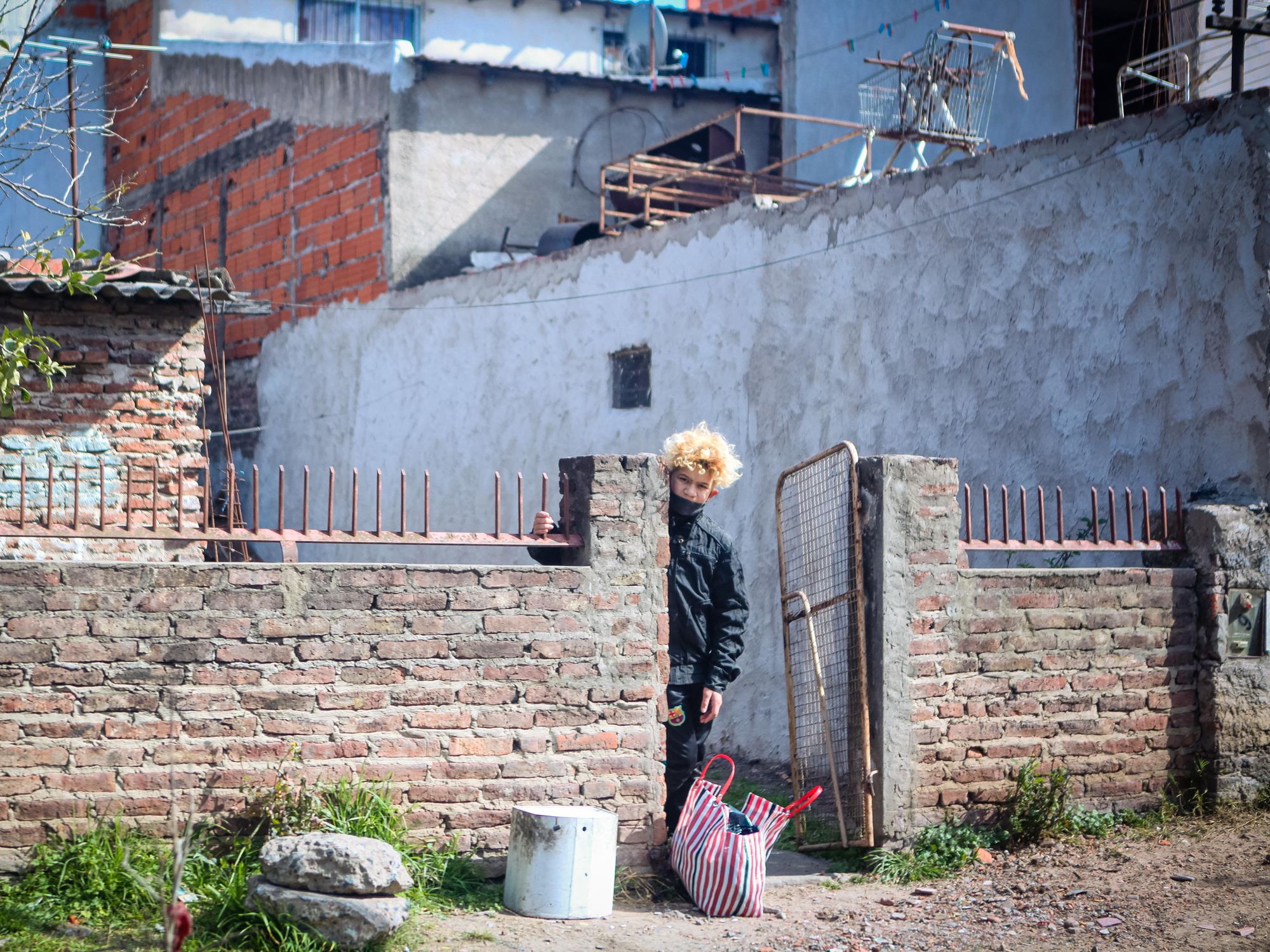 A person with blonde hair stands half hidden behind the brick wall infront of a house