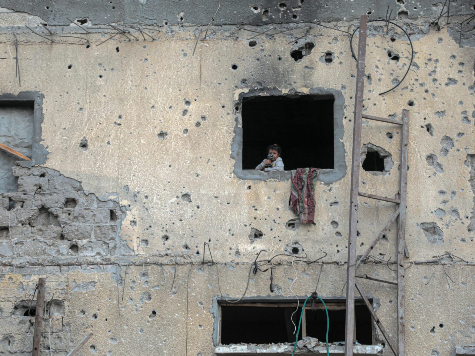a photo of a child stands by the window of a destroyed building in the southern Gaza Strip city of Khan Younis on Oct. 7, 2024