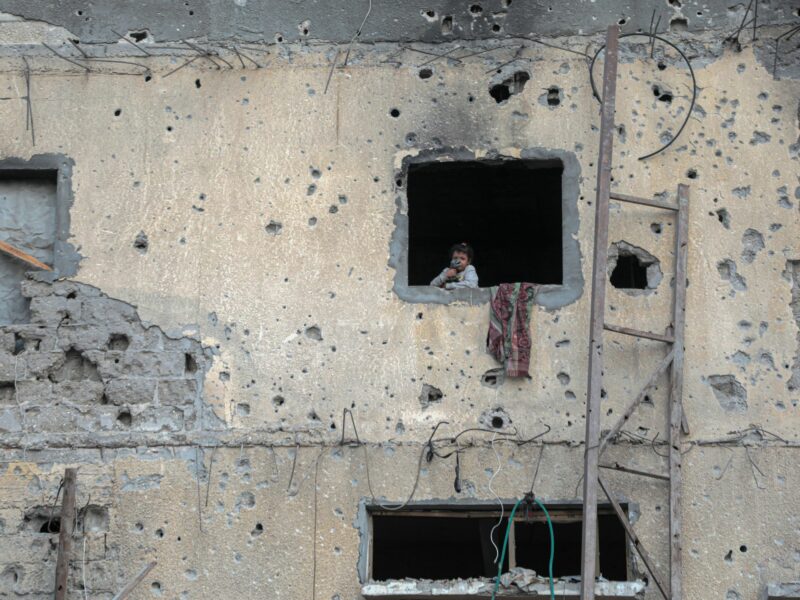 a photo of a child stands by the window of a destroyed building in the southern Gaza Strip city of Khan Younis on Oct. 7, 2024