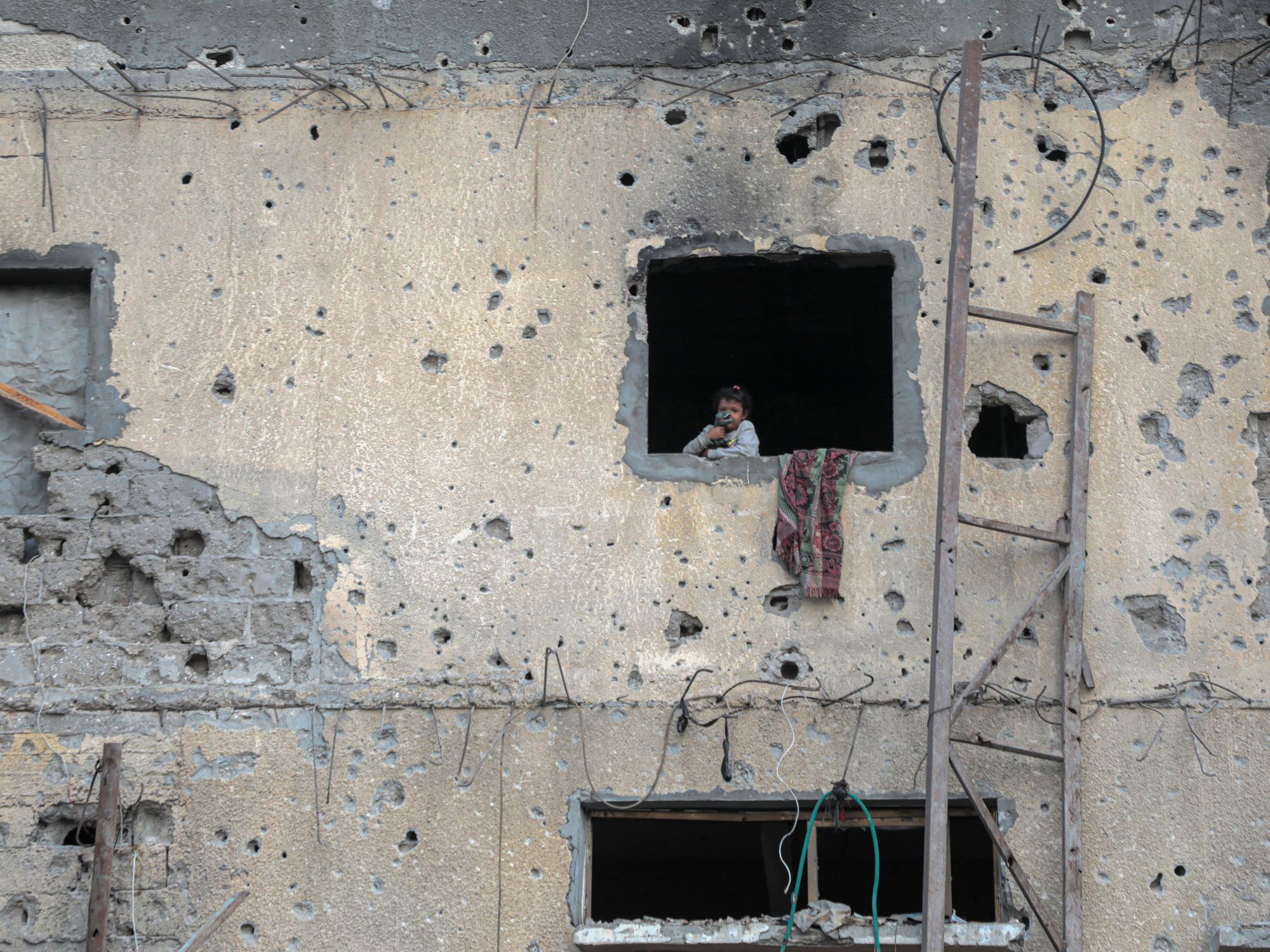 a photo of a child stands by the window of a destroyed building in the southern Gaza Strip city of Khan Younis on Oct. 7, 2024