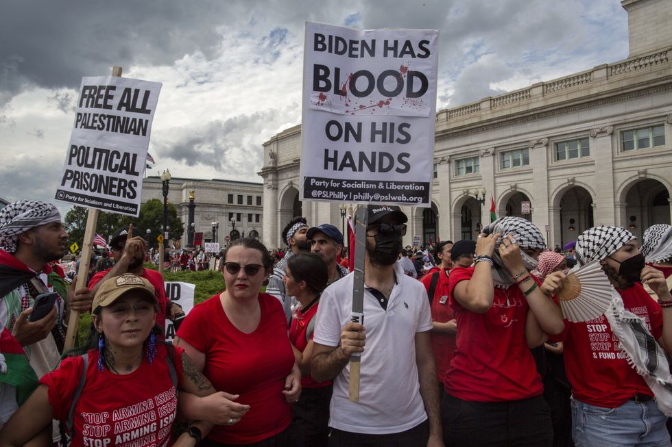A photo of A demonstrator holding a sign with Biden has blood on his hand written on it stands outside of the Union Station while joining in a demonstration.