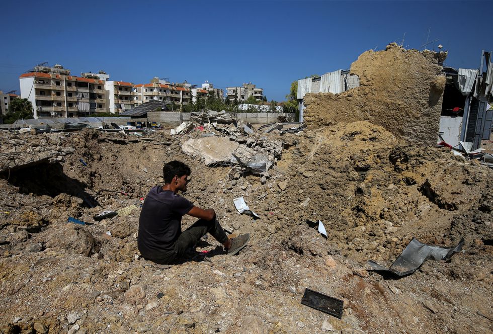A photo of a Lebanese man sitting on the edge of a crater caused by an overnight Israeli air raid attack in the area of Jiyeh along the coastal highway between the southern port city of Sidon and Beirut