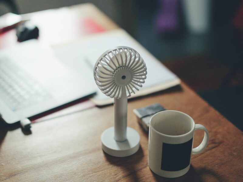 A photo of a white cup and fan on a table