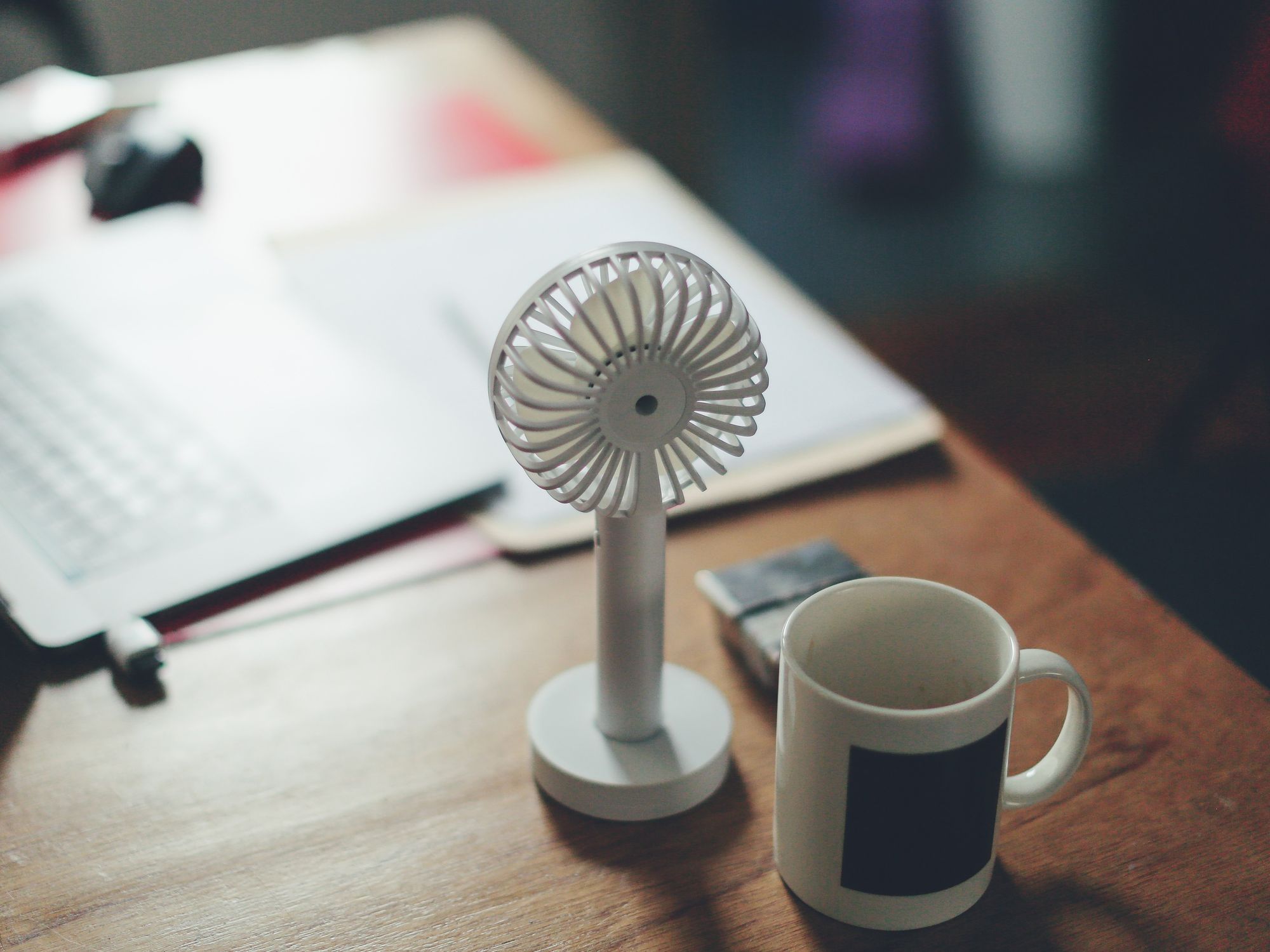 A photo of a white cup and fan on a table