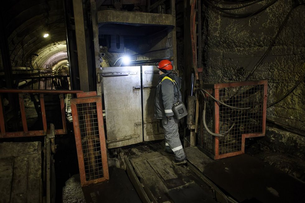 A photo of a woman miner standing next to an iron gate underground.