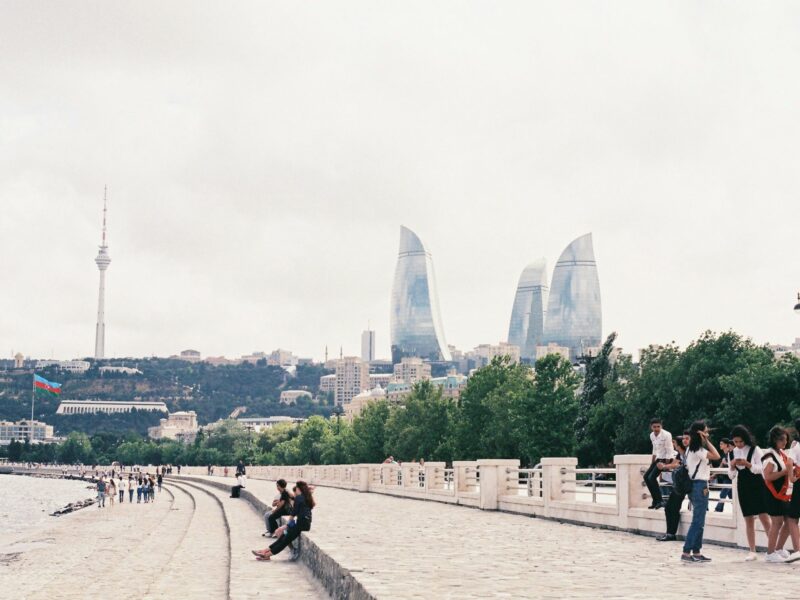 A photo of People enjoy the weather on the Baku boulevard. The iconic Flame Towers can be seen in the distance as well as the TV tower and a large flag.