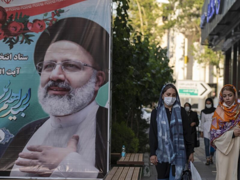 A photo of two women walking past a poster of Iran's president