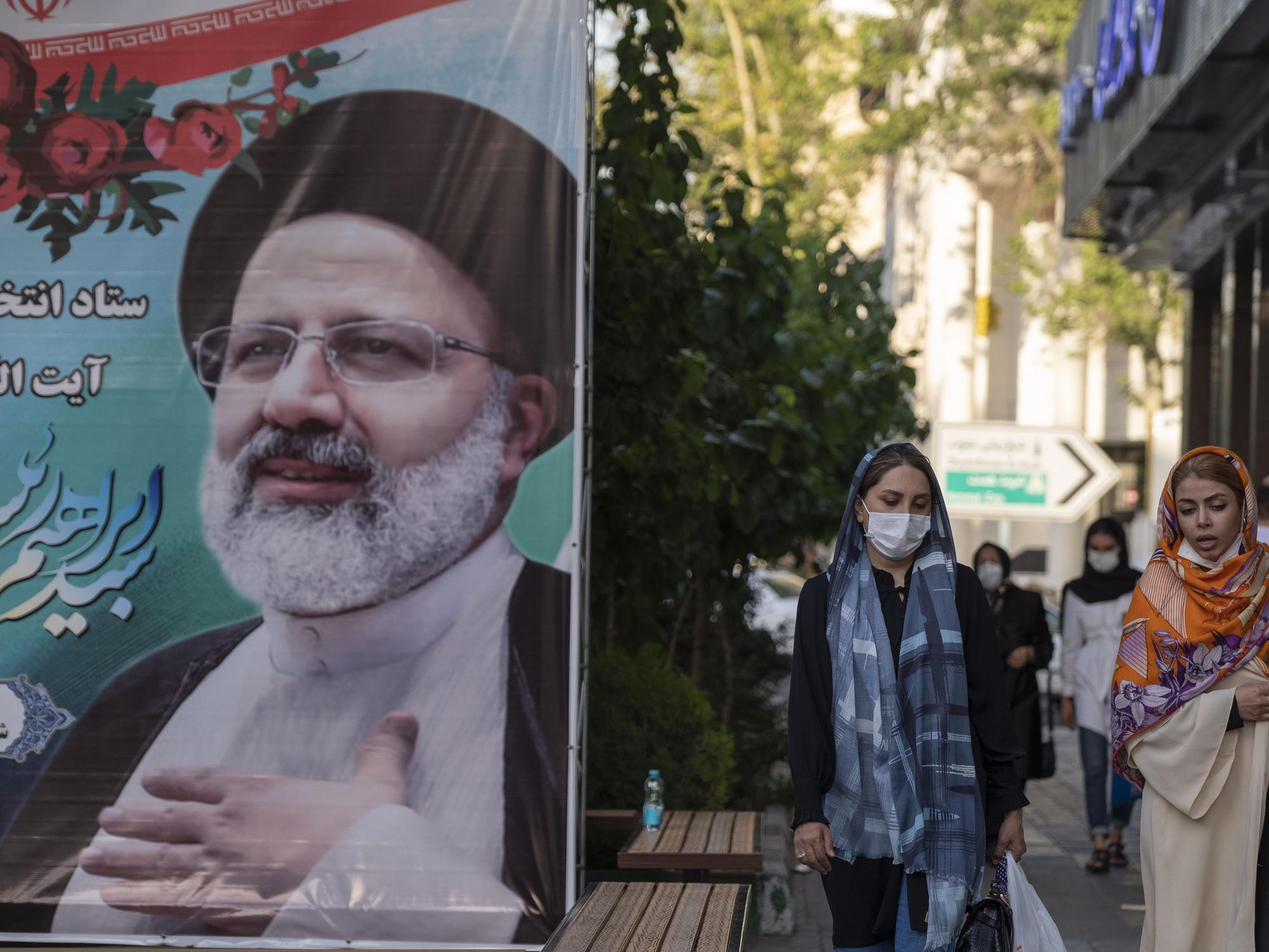A photo of two women walking past a poster of Iran's president