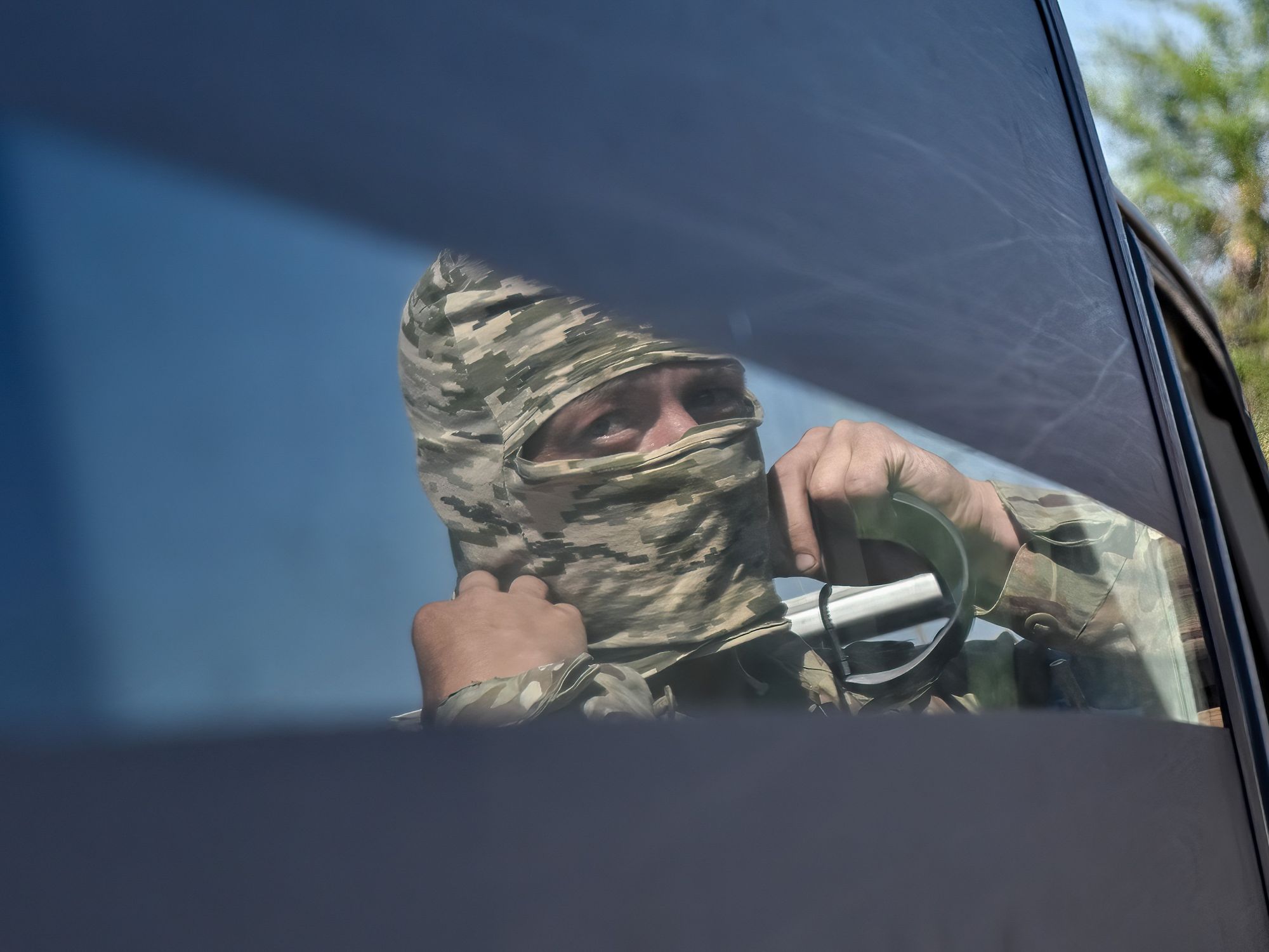 A photo of Ukrainian soldier adjusting his face mask in the reflection of a car window.