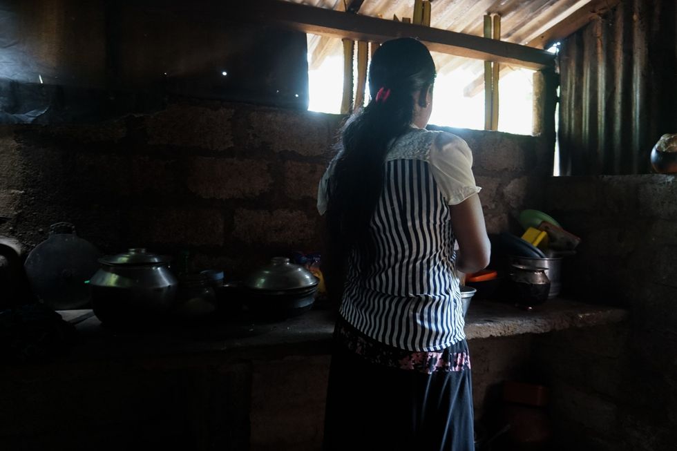 A photo of woman cleaning cookware in a dark kitchen.