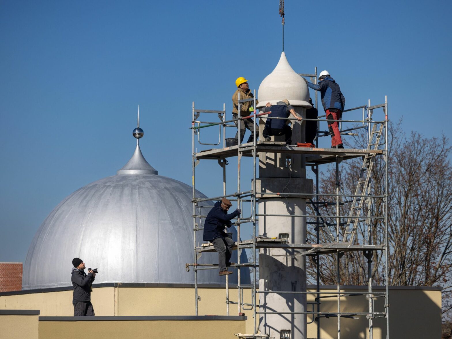 A photo of workers assembling the components of an eight-meter-heigh minaret prayer tower using a crane, part of the newly constructed Ahmadiyya mosque in Thuringia, Germany.