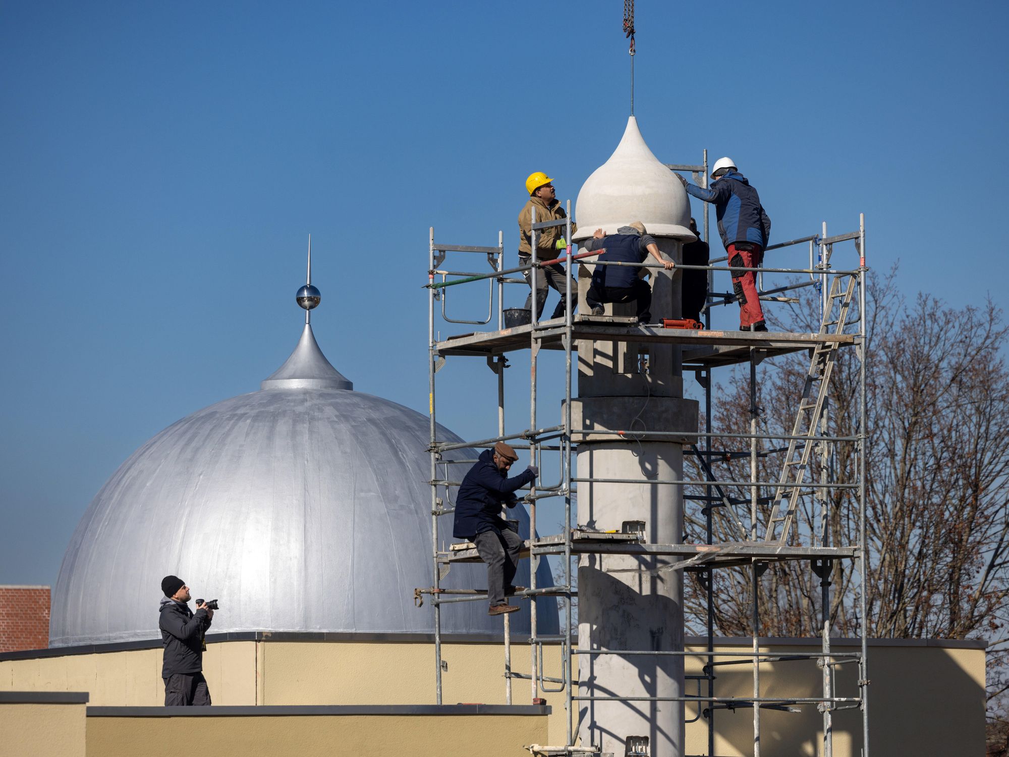 A photo of workers assembling the components of an eight-meter-heigh minaret prayer tower using a crane, part of the newly constructed Ahmadiyya mosque in Thuringia, Germany.