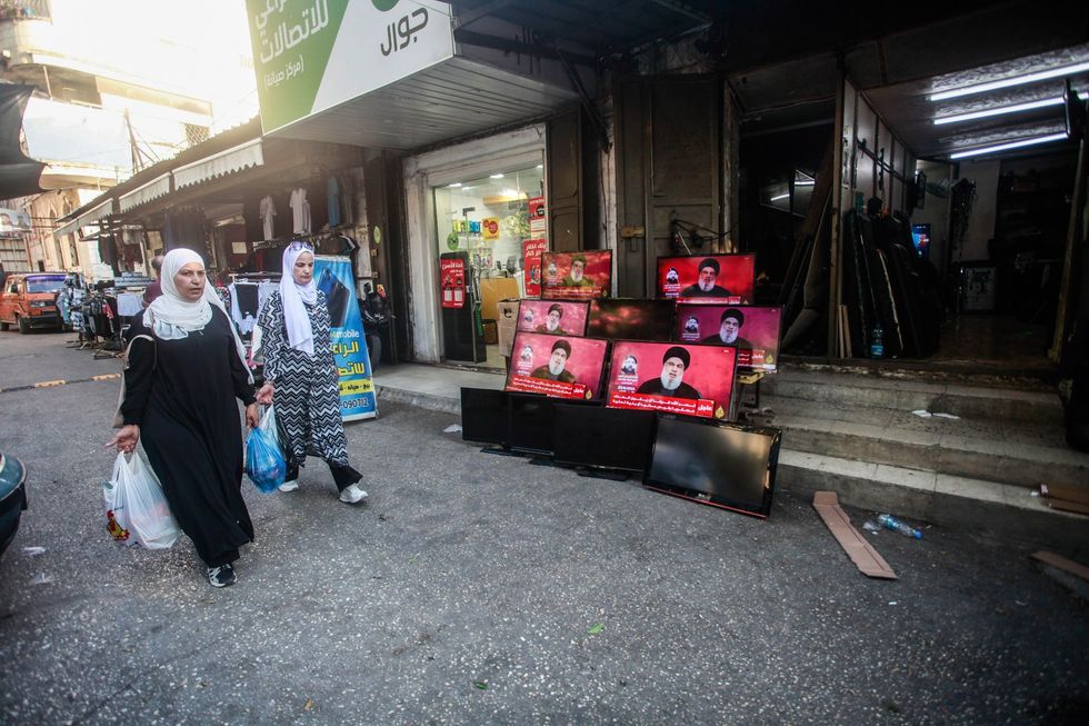 A photo Palestinians walk past TV screens broadcasting a speech by Hezbollah leader Hassan Nasrallah in Nablus, West Bank.