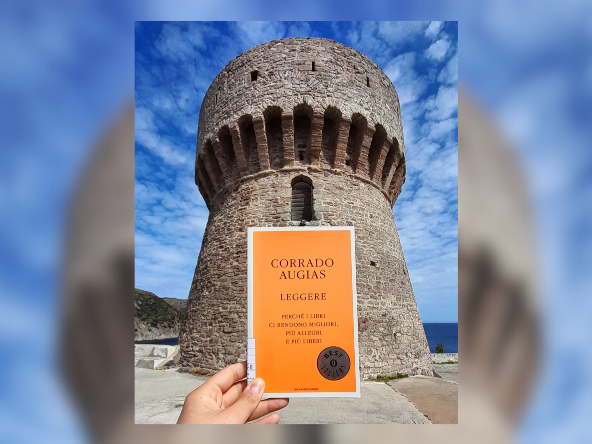 A photograph of a book about the importance of reading, held up against the tower of Capraia's library