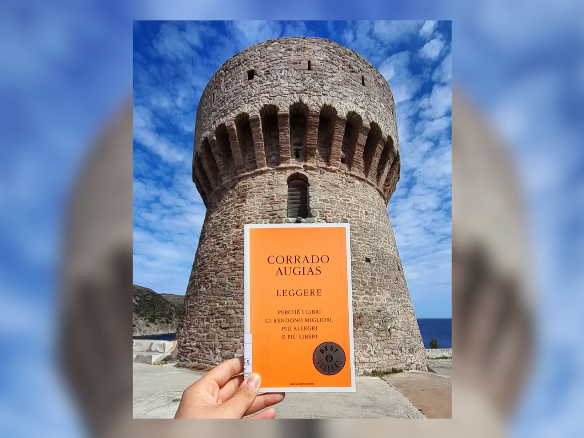A photograph of a book about the importance of reading, held up against the tower of Capraia's library