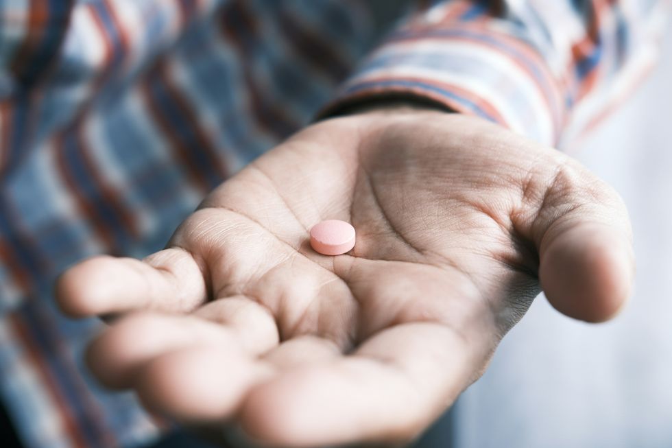 A photograph of someone handing a pink pill.