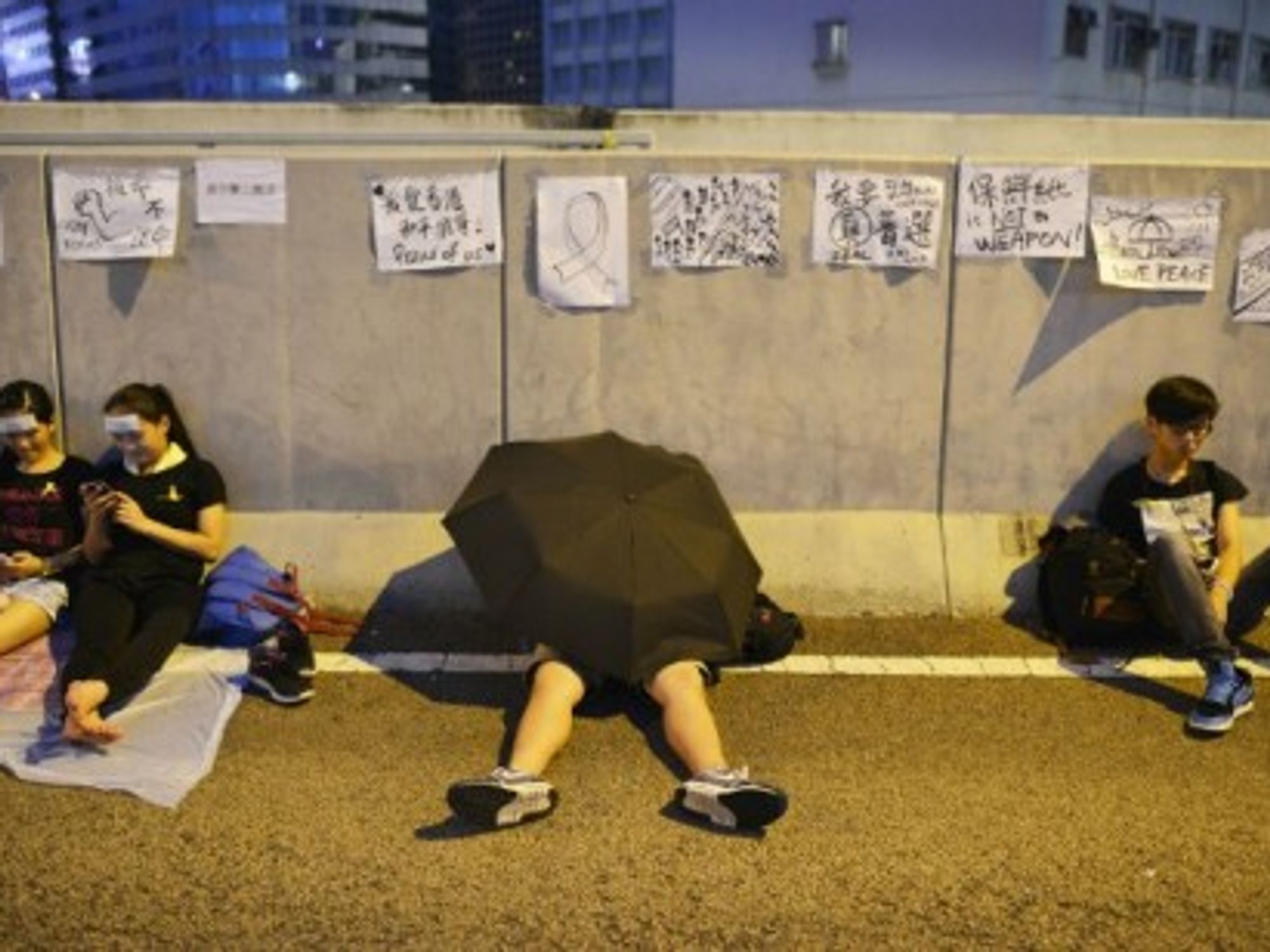 A pro-democracy protestor rests under an umbrella.