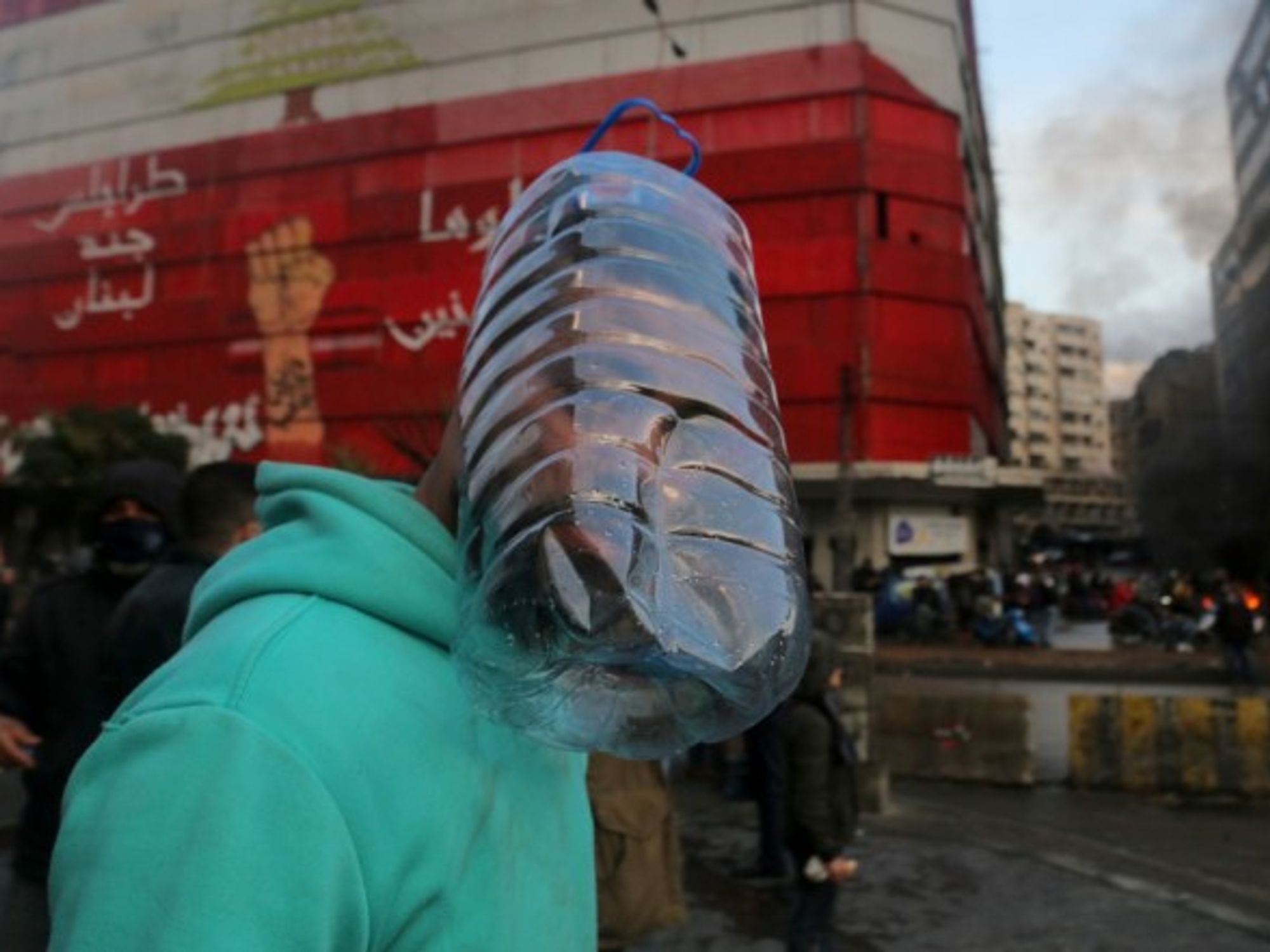 A protester uses a plastic water container as a mask to protect him from tear gas during a demonstration in Tripoli, Lebanon, against the national lockdown and the worsening economic conditions.