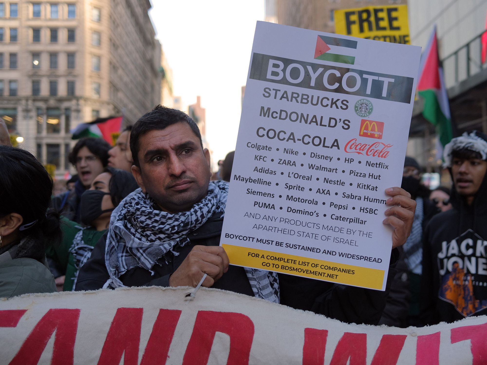 A protestor wearing the Palestinan keffiyah holding up a BDS sign with a list of companies to boycott.