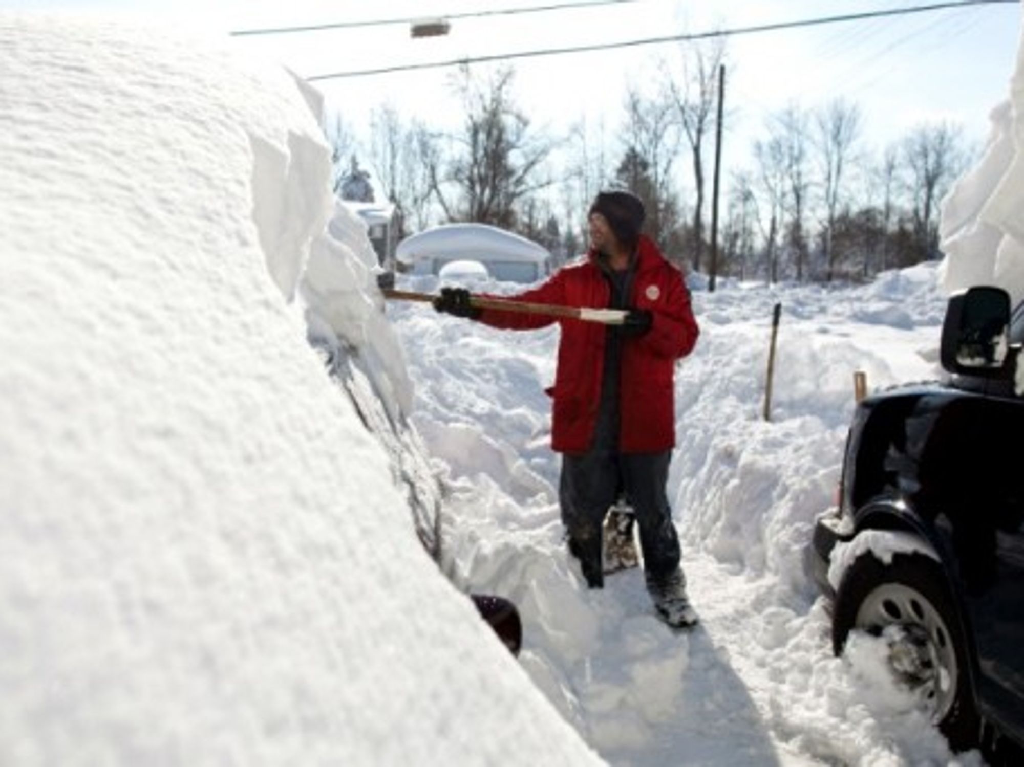 A resident of Alden, New York, shovels snow from atop his car.