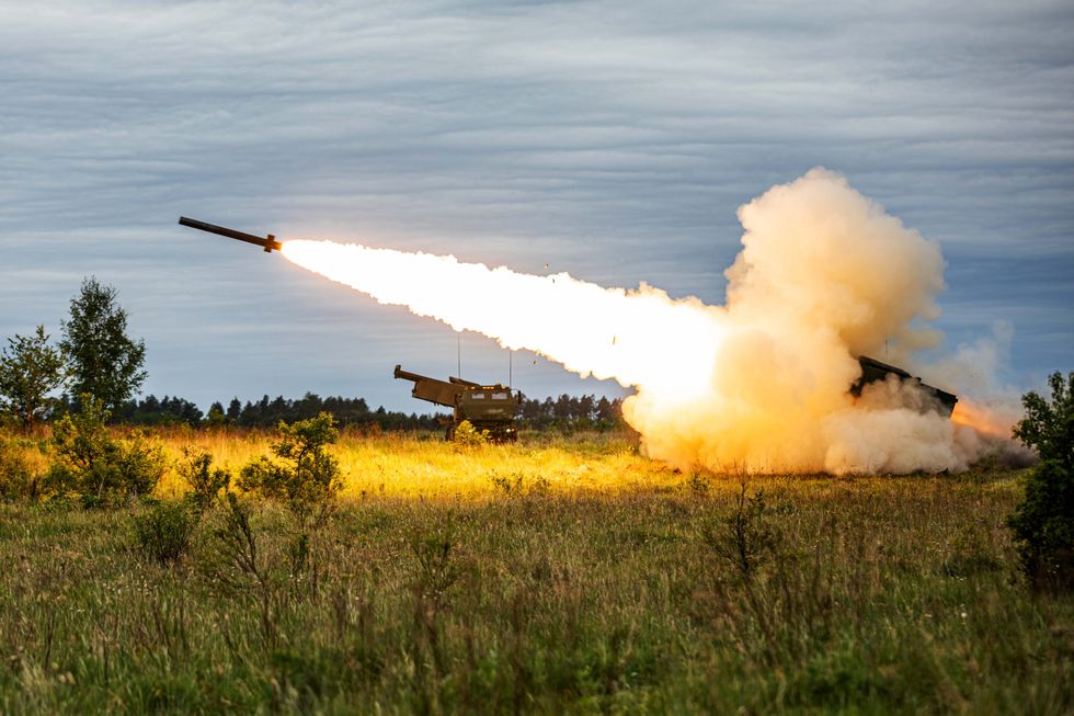 a rocket takes off from truck-mounted artillery in the middle of a green and yellow field.