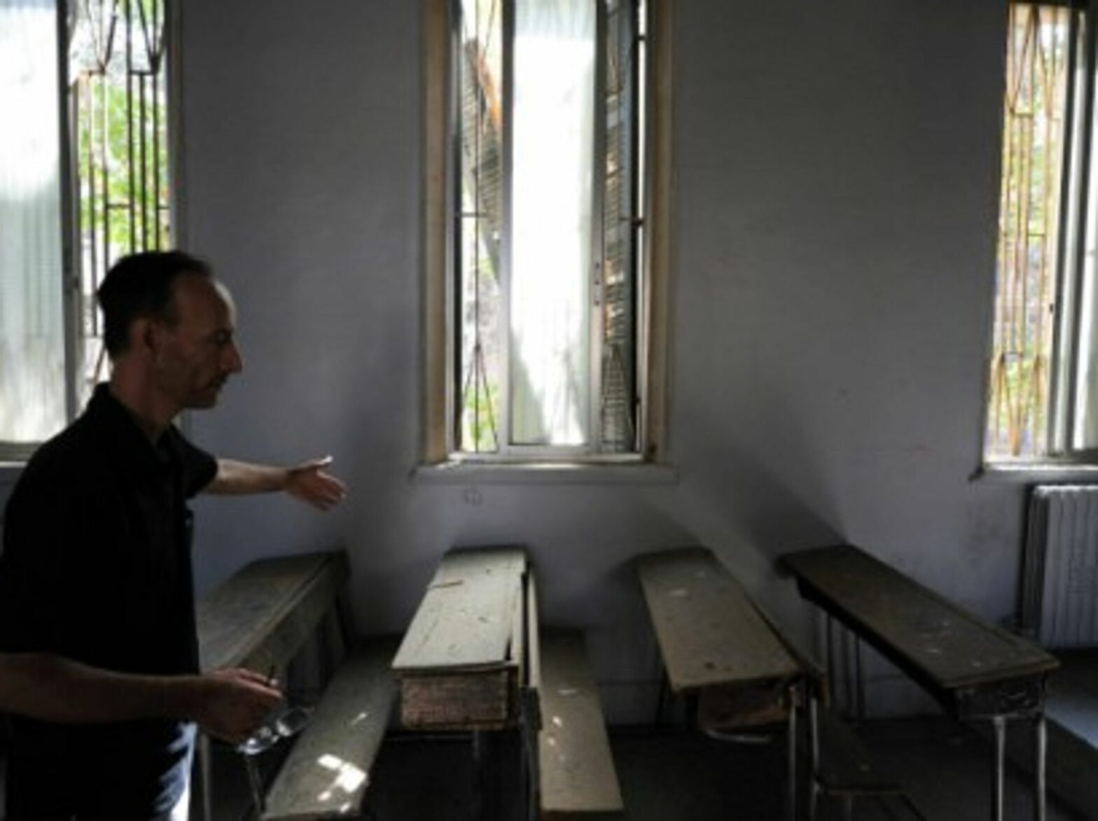 A school worker shows a classroom damaged by a mortar shell in Damascus