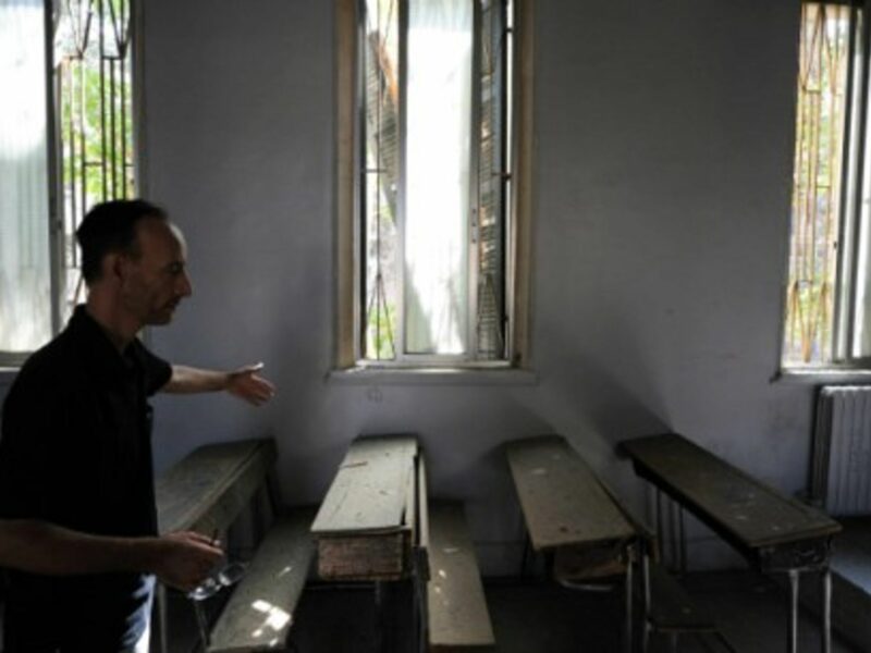 A school worker shows a classroom damaged by a mortar shell in Damascus