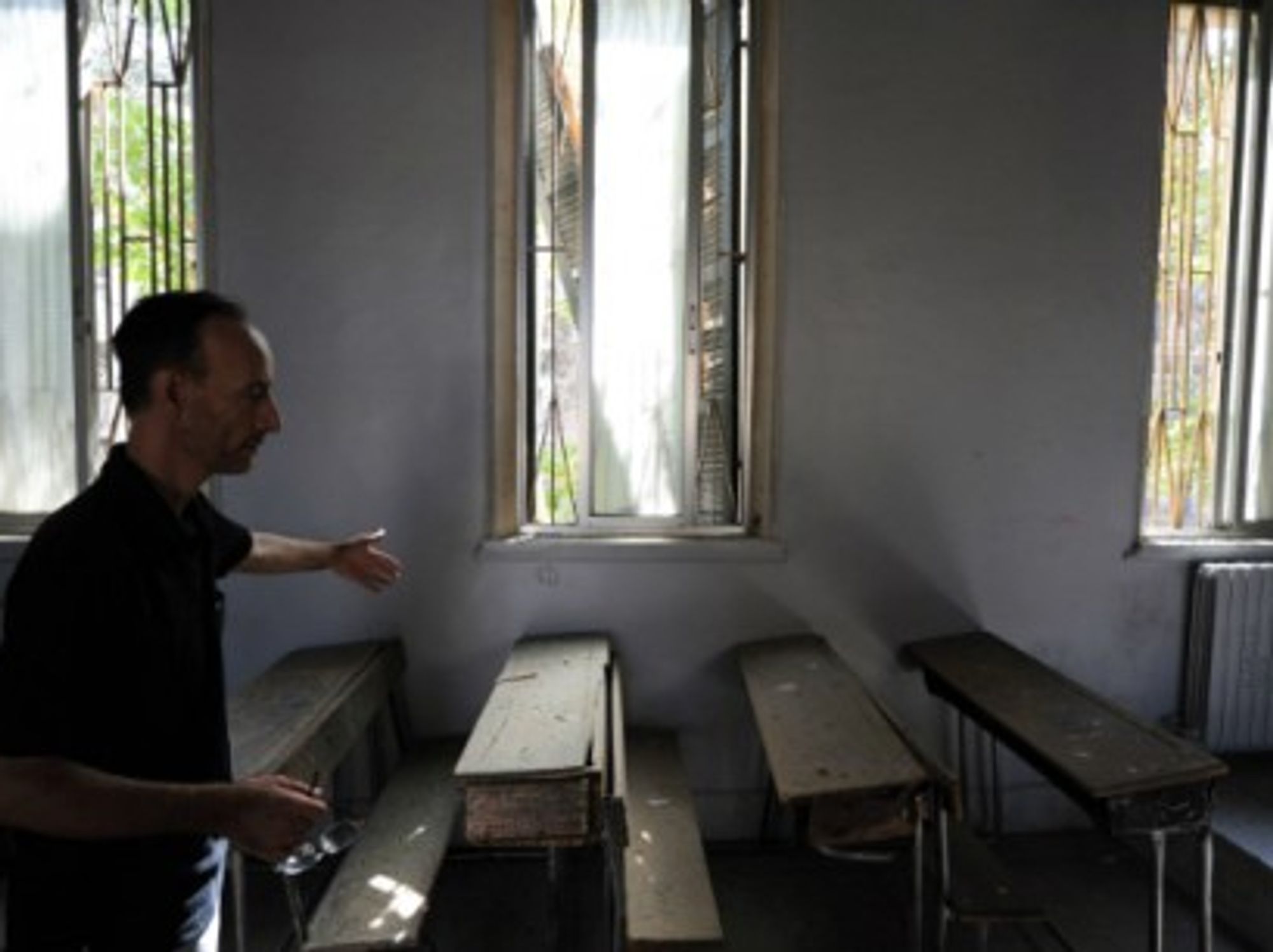 A school worker shows a classroom damaged by a mortar shell in Damascus