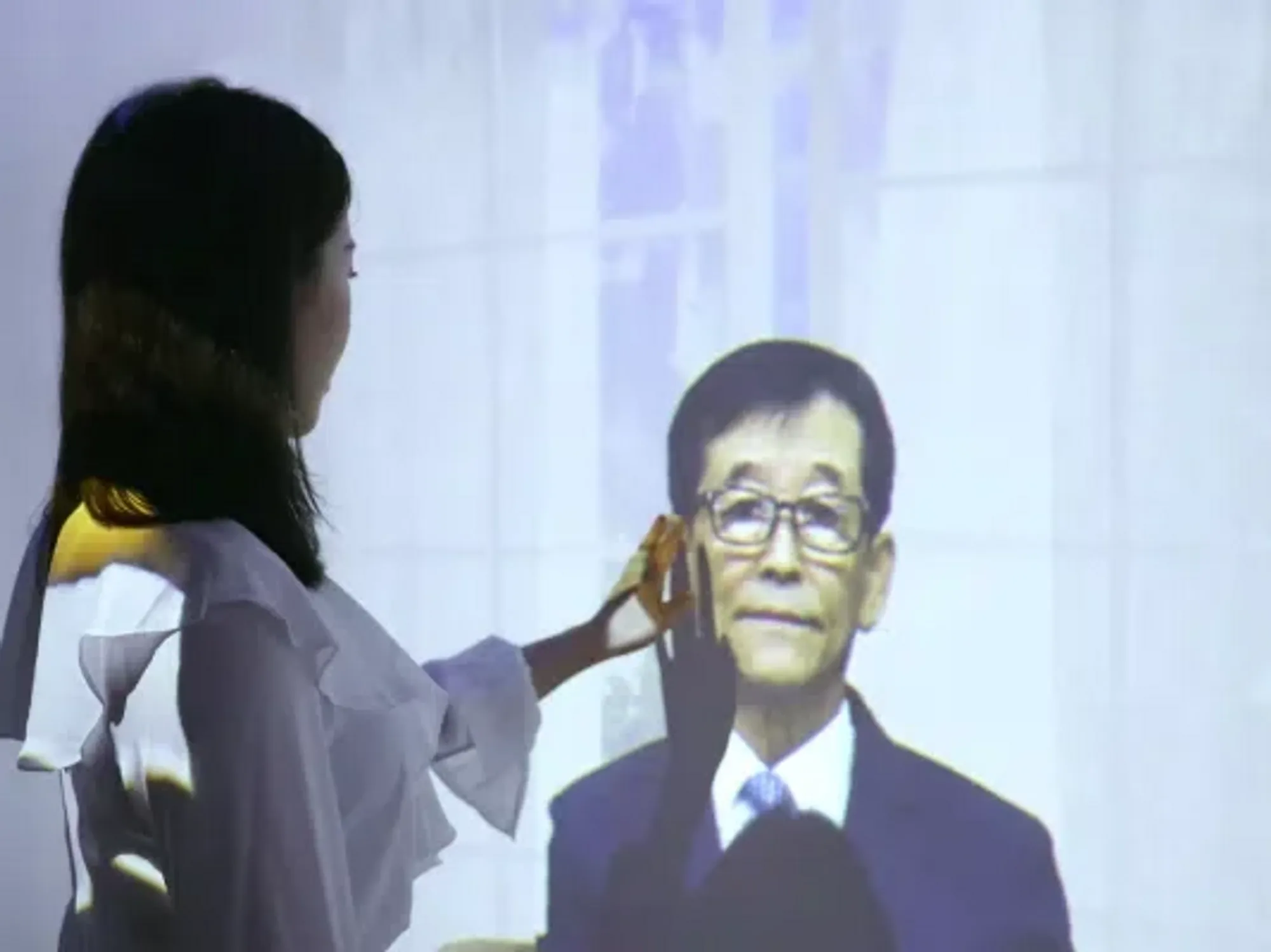 A screenshot from the Re;memory promotional video, where a bereaved woman touches the screen that shows her dead relative talking to her