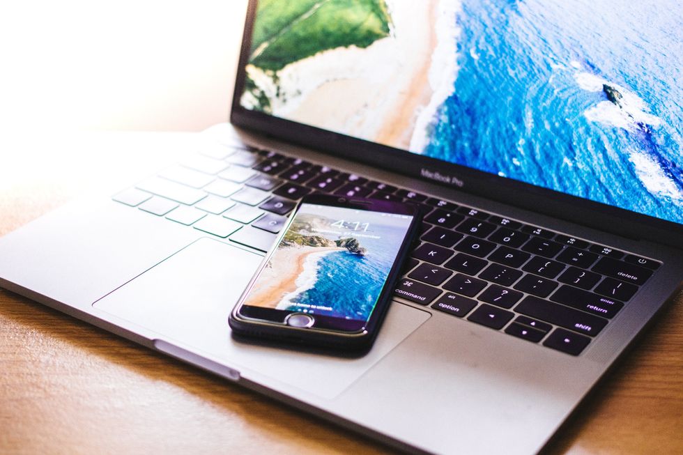 a smartphone with a beach scenery on top of the keyboard of a laptop with a beach scenery on screen