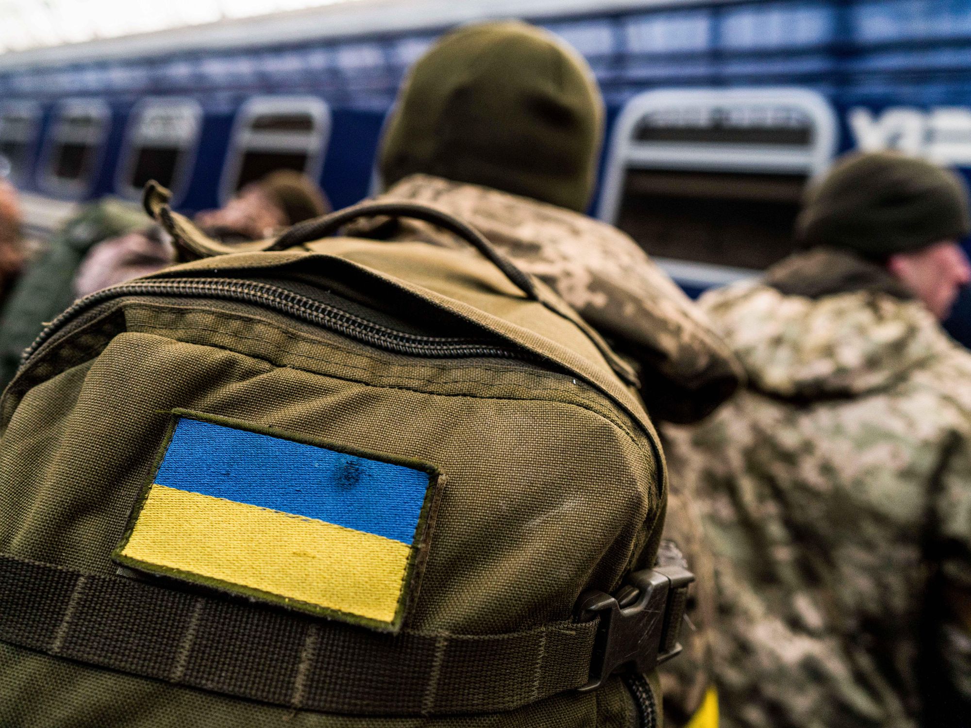 a soldier carrying a military backpack with the Ukrainian flag sewn to it watches a train arrive in Lviv station