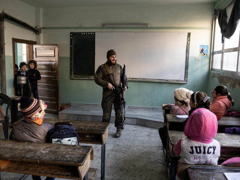 A soldier stands at the front of a classroom with young children