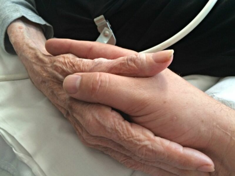 A son holding his mother's hand in a palliative care facility in Oakland, United States on June 26, 2015