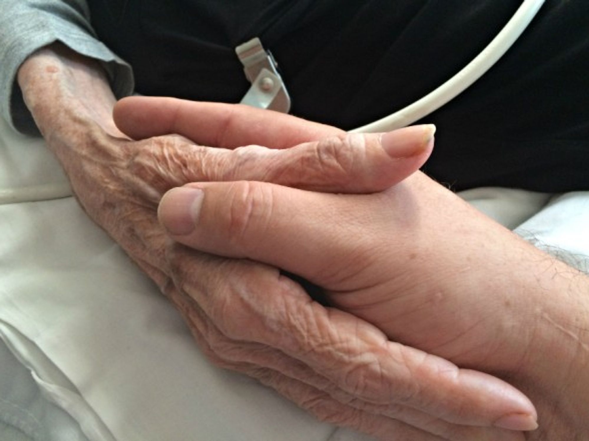 A son holding his mother's hand in a palliative care facility in Oakland, United States on June 26, 2015
