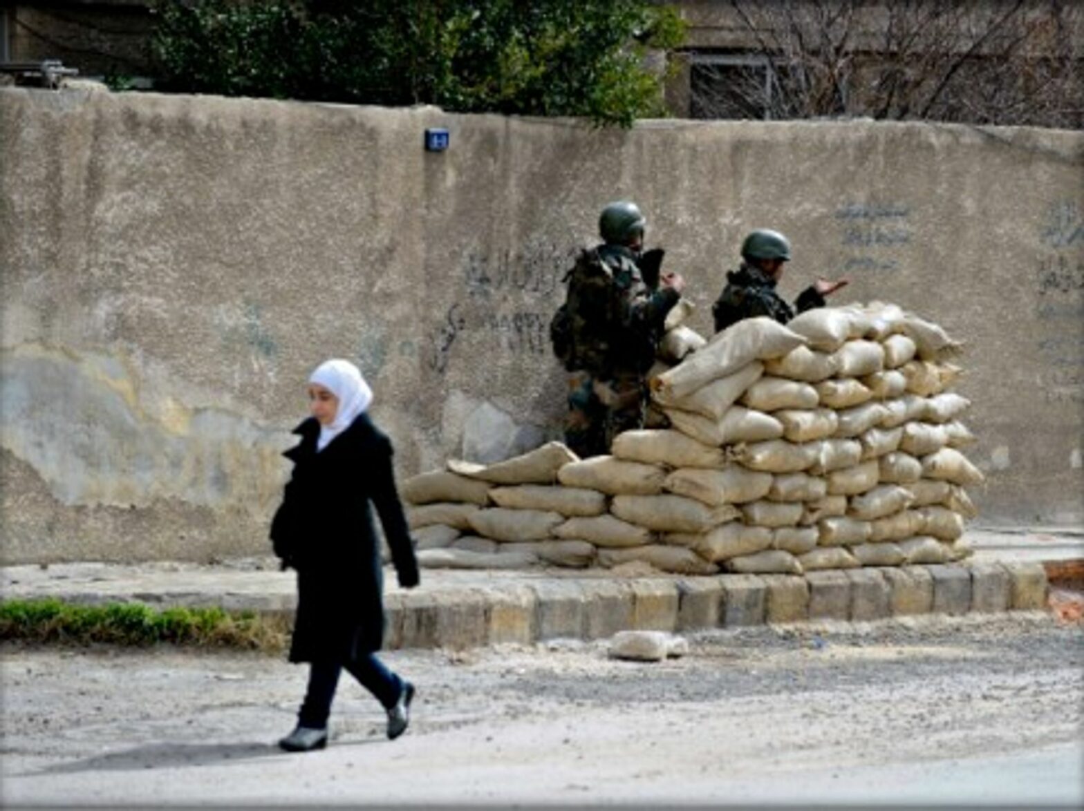A Syrian girl walks past Syrian army soldiers in Harasta, near Damascus