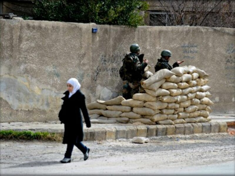 A Syrian girl walks past Syrian army soldiers in Harasta, near Damascus