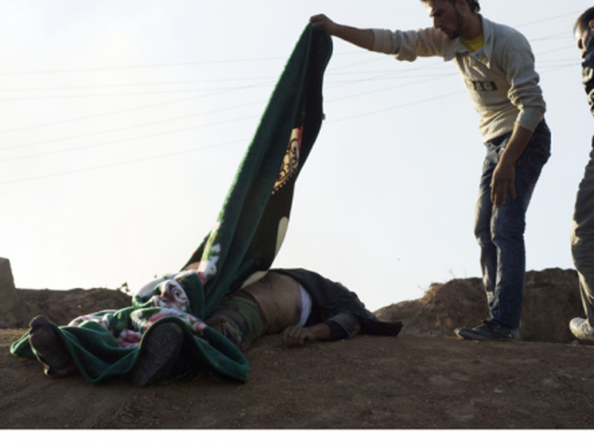 A Syrian man covers a dead Syrian army soldier with a blanket after a battle last year near Ras al Ayn, Syria