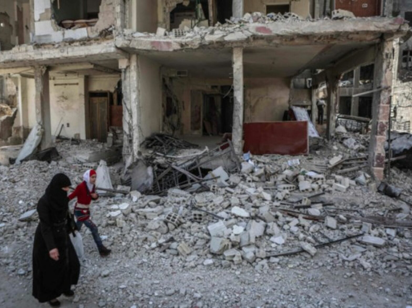 A Syrian woman and her daughter walk past a destroyed house in the rebel-held Eastern Al-Ghouta province.