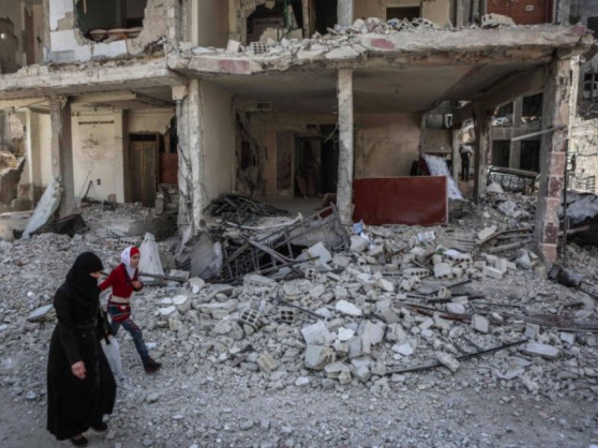 A Syrian woman and her daughter walk past a destroyed house in the rebel-held Eastern Al-Ghouta province.