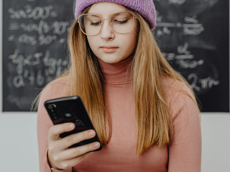 A teenage girl is on her phone in front of a blackboard