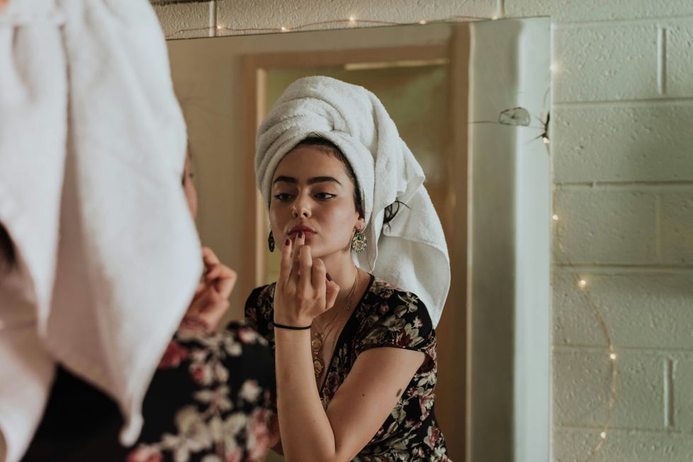 A teenager applies her lipstick in a bathroom mirror.