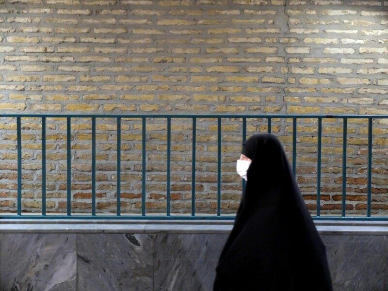 A veiled woman is walking along a guardrail in Tehran