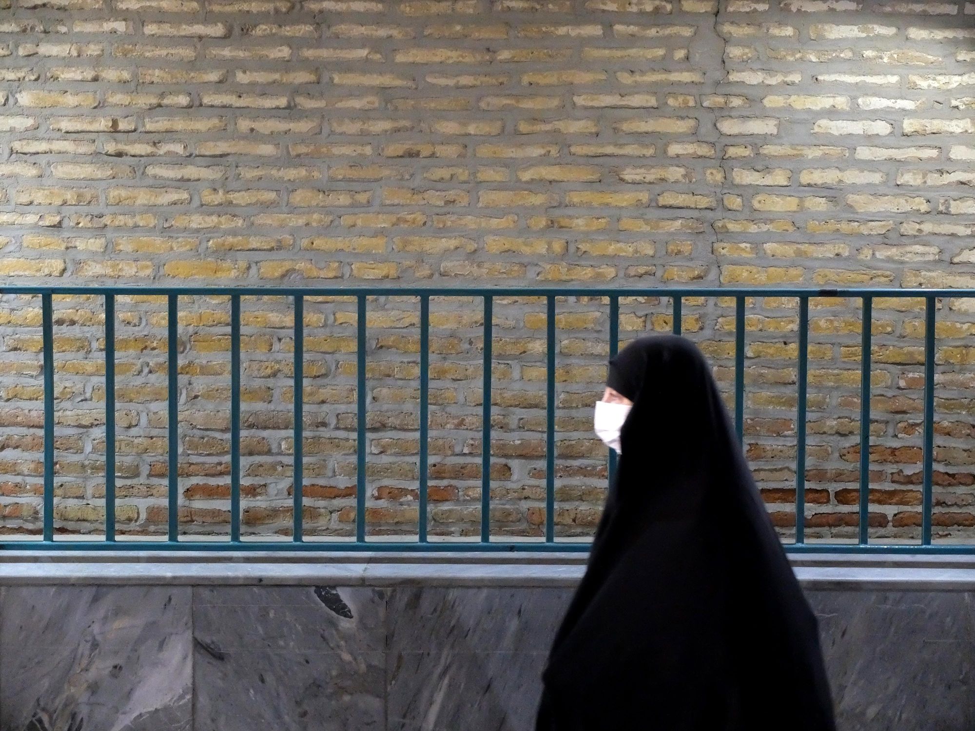 A veiled woman is walking along a guardrail in Tehran