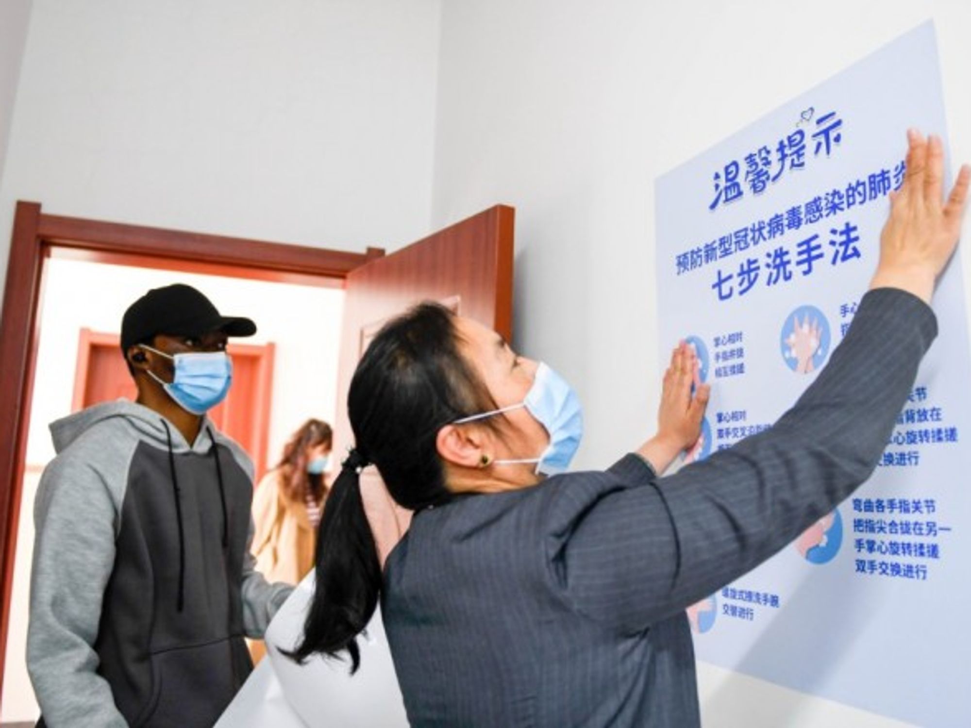 A visiting medical student watches a teacher to post anti-epidemic poster in Changchun University.
