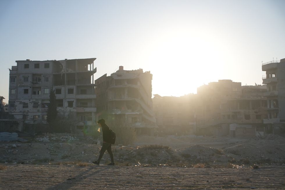A walk walks past destroyed buildings as the sun sets in the Syrian capital city Damascus on December 19, 2024
