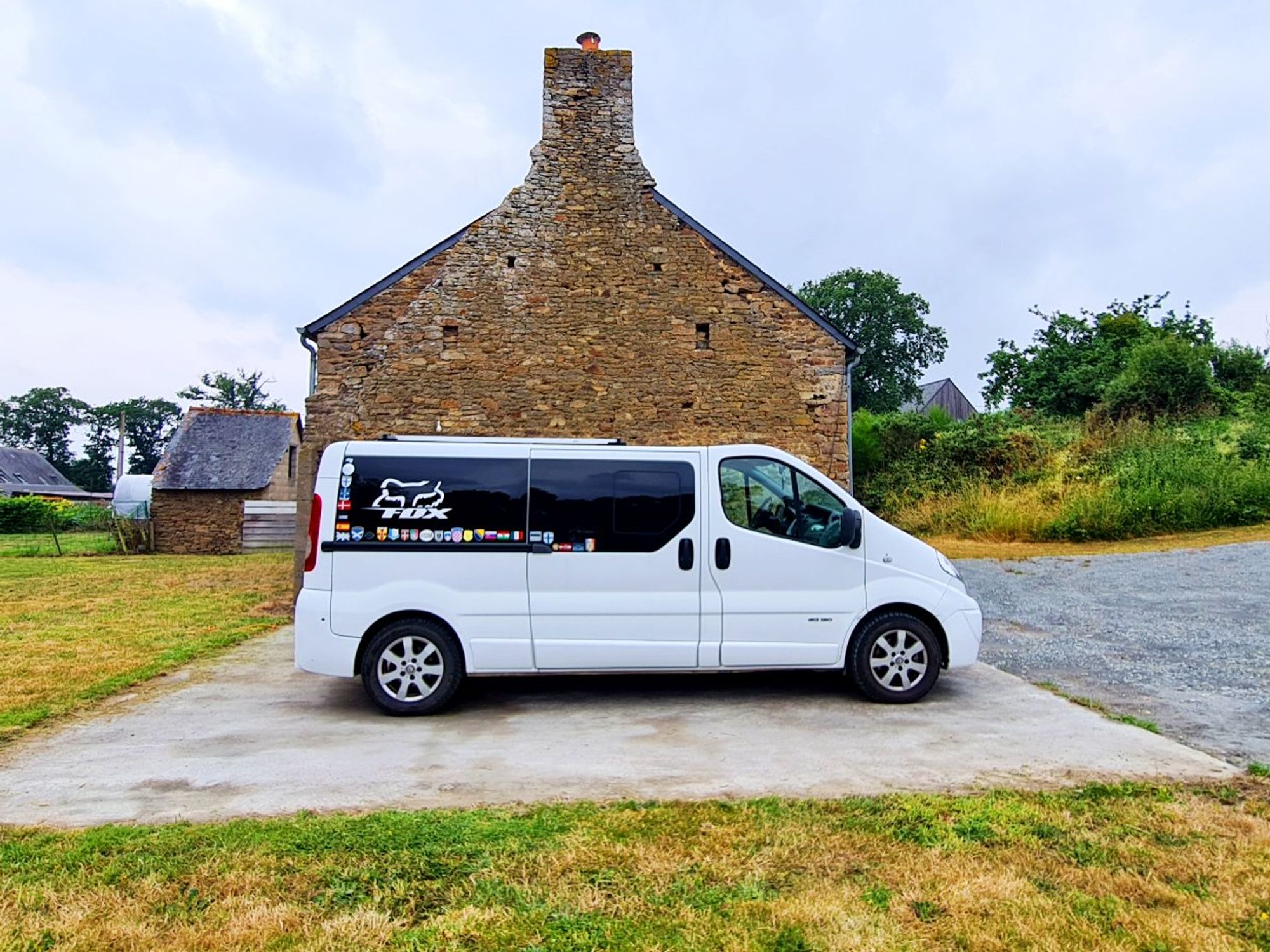 A white campervan in parked besides a stone house