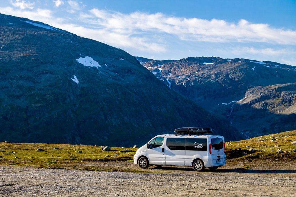 A white van parked infront of moutains lightly specked with snow