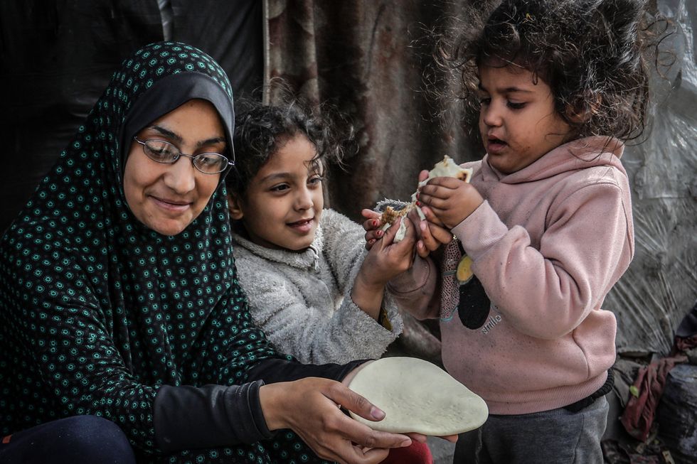 A woman feeding naan bread to her two daughters at a temporary camp in Rafah