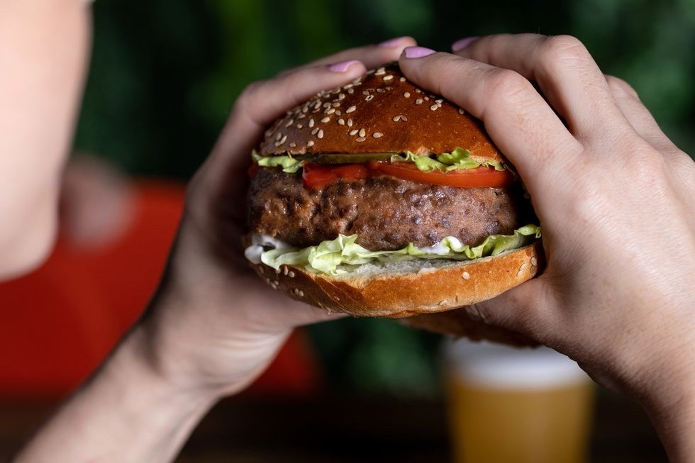 A woman holds a burger made with meat grown from animal cells.
